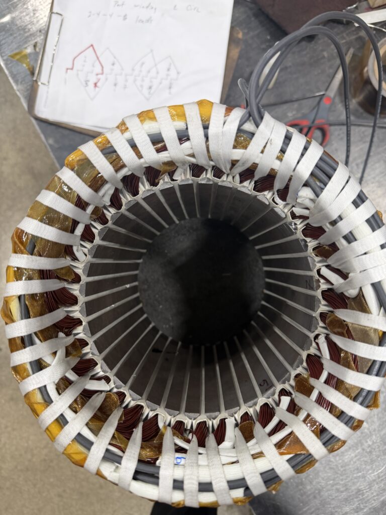 Stator during rewinding, end turns laced, with the winding diagram on the bench